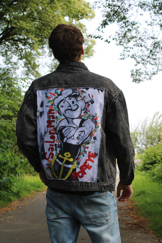 Black denim jacket featuring a striking black-and-white painting of the Sailor Man on the back, with magazine clippings for added texture.