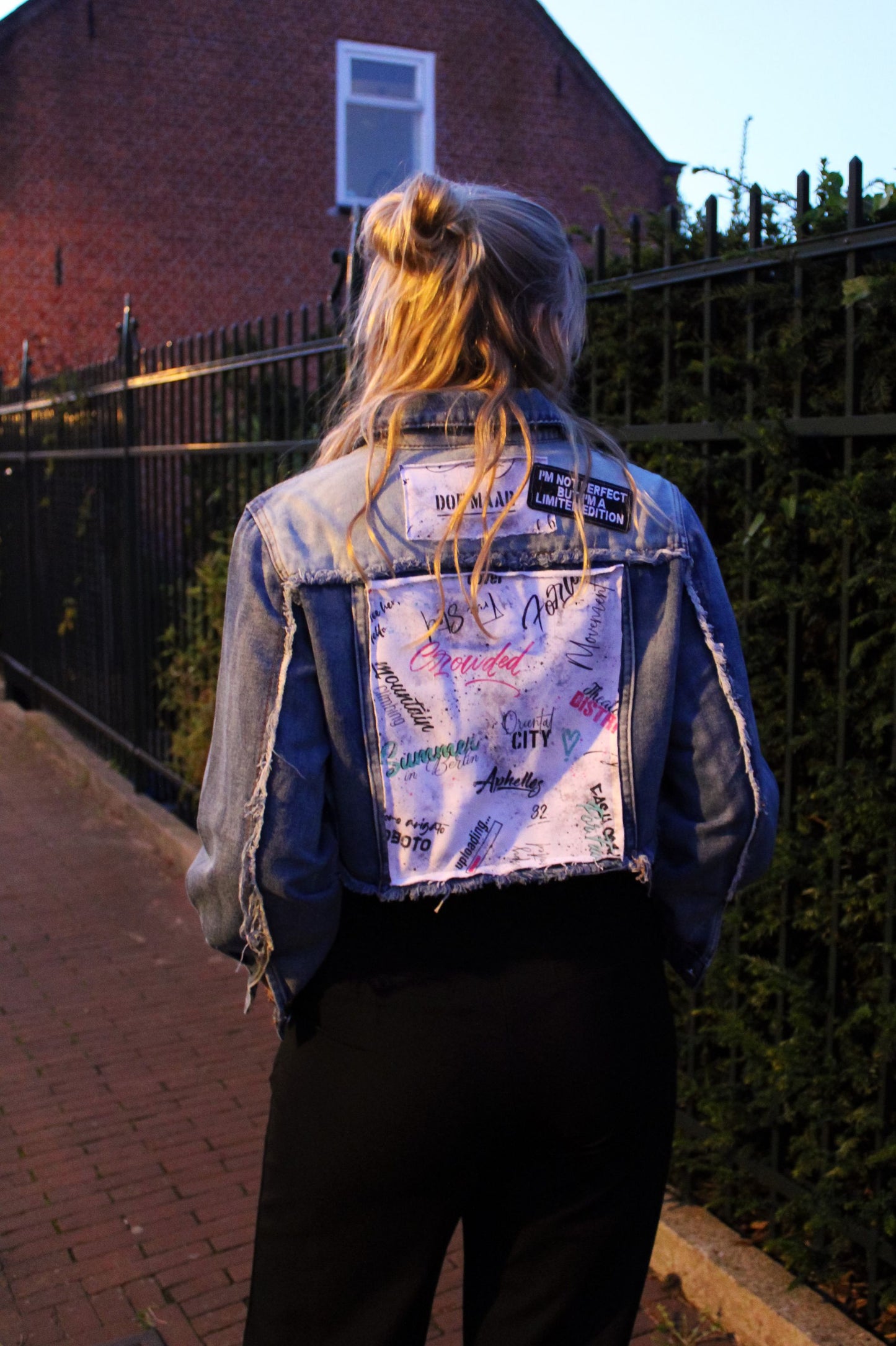 Bold, fashion-forward denim jacket with a cropped fit and striking stitched-on text panels in black, white, pink, and green accents.