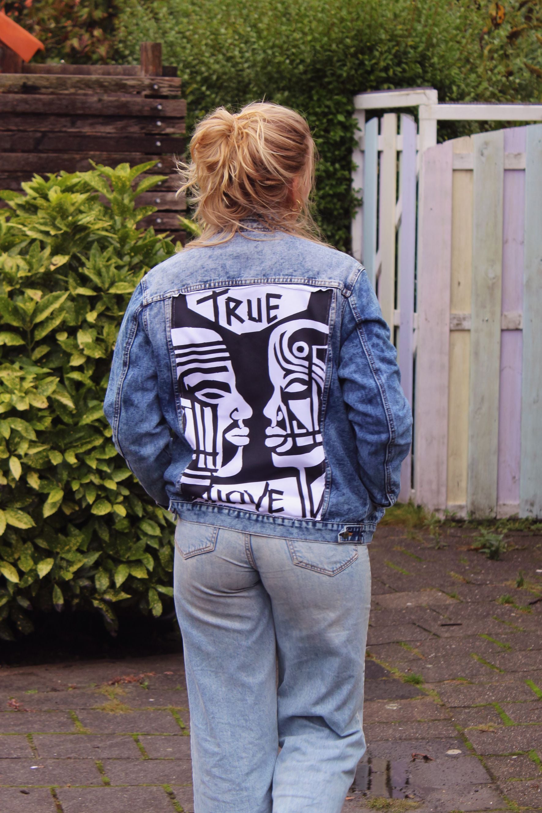 Wearable art jean jacket with a relaxed fit, textured details, and a striking face design.