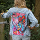 a light blue womens jacket with a striking pink, orange and redish color scheme panel on the back